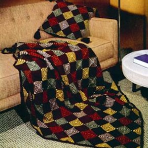May include: A crocheted blanket and cushion set featuring a geometric design of squares in red, black, yellow, and green. The blanket is draped over a beige sofa, and the cushion has tassels.