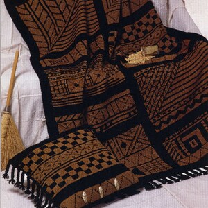 May include: A brown and black patterned blanket and cushion set. The blanket and cushion feature geometric designs and a black border. The cushion has decorative gold-coloured buttons and fringe.