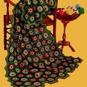 May include: A green crochet blanket with a scalloped edge and a repeating pattern of colorful flowers. The blanket is draped over a wooden chair.