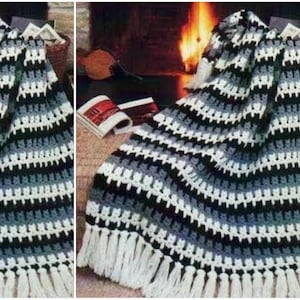 May include: A crocheted blanket with a striped pattern in black, white, and gray. The blanket has a fringe border and is draped over a chair in front of a fireplace.