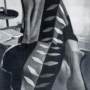 May include: A black, white, and gray knitted throw blanket with a leaf pattern. The blanket is draped over a chair.