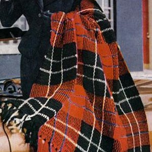 Pode incluir: Uma manta de crochê xadrez vermelha, preta e branca com franjas nas bordas.