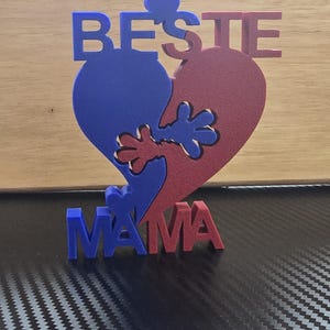 Puede incluir: Un letrero de madera en forma de corazón azul y rojo con las palabras "BESTIE MAMA" en él. El corazón está dividido en dos mitades con una mano que sale de cada lado.
