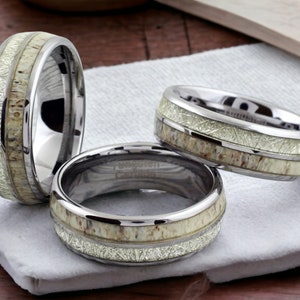 May include: Three silver tungsten carbide rings with a white antler inlay. The rings are stacked on top of each other.