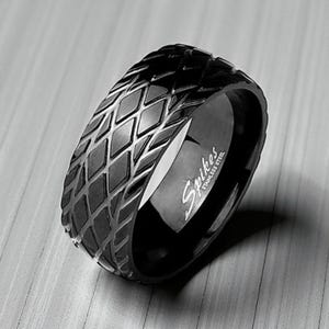 May include: A black stainless steel ring with a diamond pattern around the band. The ring has the word "Spikes" engraved on the inside. The ring is a dark, shiny black color.
