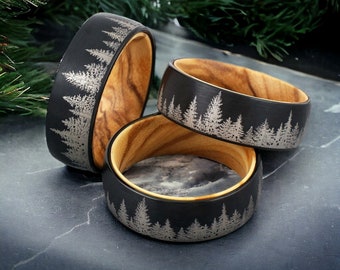 May include: Three black tungsten carbide rings with a wood inlay. Each ring features a silver etched design of a forest tree line.