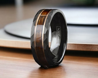May include: A black tungsten ring with a brown wood inlay and a faceted design. The ring is engraved with the word "Tungsten".
