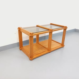 May include: A light brown wooden coffee table with two glass tops. The table has a rectangular shape with a lower shelf. The design is simple and modern, suitable for a living room.