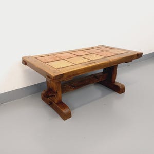 May include: A rustic wooden coffee table with a top made of terracotta tiles. The table has a simple, sturdy design with a rectangular top and four legs.