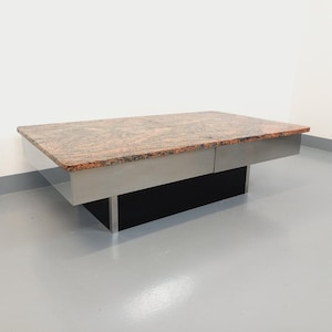 May include: A modern coffee table with a rectangular granite top and a stainless steel base. The base has two drawers and a black shelf.