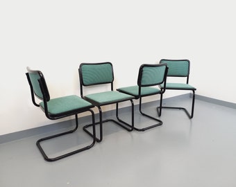 May include: Four black metal chairs with green fabric seats. The chairs are arranged in a row, with the backs of the chairs facing the viewer.