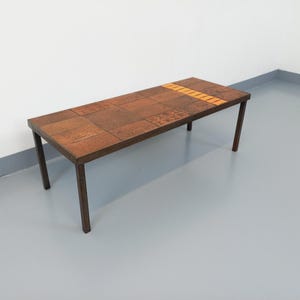 May include: A mid-century modern coffee table with a wood veneer top and a metal frame. The top is made of small squares of wood in different shades of brown, with a band of lighter wood running down the center.