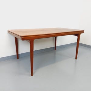 Könnte beinhalten: Ein rechteckiger Holztisch mit warmbraunem Finish. Der Tisch hat vier angewinkelte Beine und ein schlichtes, minimalistisches Design. Die Abmessungen des Tisches betragen ca. 122 cm lang, 76 cm breit und 71 cm hoch.