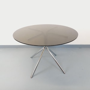 May include: A modern, round coffee table with a smoked glass top and a chrome, three-legged base. The table's diameter is approximately 36 inches.