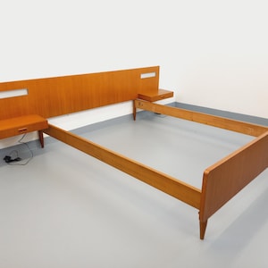 May include: A mid-century modern wooden bed frame with a headboard and two attached nightstands. The headboard has a rectangular cutout. The bed frame is made of light brown wood and has a minimalist design.