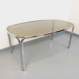 May include: A modern, oval-shaped coffee table with a smoked glass top and chrome legs. The table has a sleek, minimalist design, perfect for a living room or lounge area. The table is approximately 60 inches long, 30 inches wide, and 16 inches high.