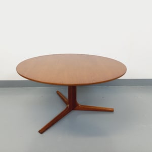 May include: A mid-century modern round coffee table. The table has a light brown wooden top and a three-legged base. The table is approximately 30 inches in diameter and 16 inches tall.