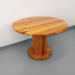 Peut inclure: Une table ronde en bois avec un plateau en bois massif et un piétement cylindrique. La table est en bois naturel avec une finition brun clair.