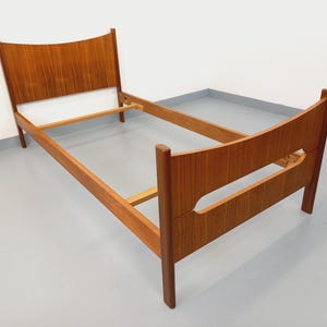 May include: A mid-century modern wooden bed frame with a headboard and footboard. The bed frame is made of light brown wood and has a simple, elegant design. The headboard is curved at the top.