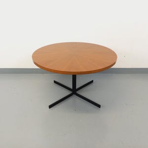 May include: A round wooden table with a light brown surface and a black metal base. The table is approximately 36 inches in diameter and has a starburst pattern on the tabletop. The base has four legs.