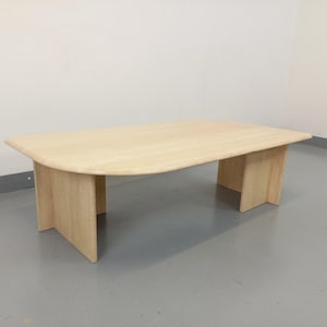 May include: A light wood oval coffee table with a curved edge and a simple design. The table has four legs that are attached to the underside of the table top.