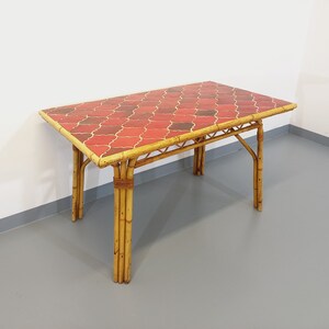 May include: A rectangular table with a red and gold tiled top and a bamboo frame. The table has a simple design with four legs.