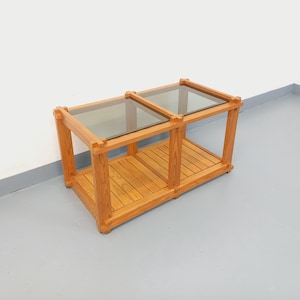 May include: A light brown wooden coffee table with two glass tops and a lower shelf. The table has a rectangular shape and is made of wood. The glass tops are tinted. The table is suitable for a living room.