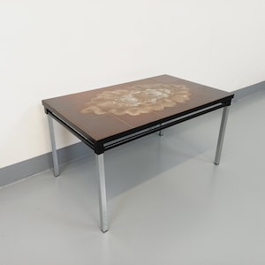 May include: A mid-century modern coffee table with a brown tiled top featuring a geometric pattern. The table has a black metal frame with silver legs.