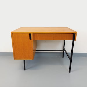 Może przedstawiać: Biurko w stylu mid-century modern z jasnym wykończeniem z usłojeniem drewna. Biurko posiada prostokątny blat, szafkę po lewej stronie i czarne metalowe nogi. Biurko ma około 122 cm szerokości i 61 cm głębokości.