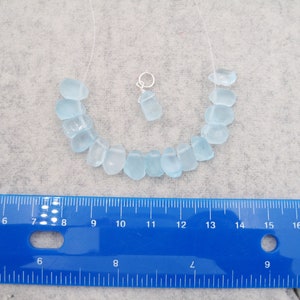 May include: A light blue sea glass necklace with a silver charm. The necklace is approximately 10 inches long and the beads are about 1/2 inch in diameter.