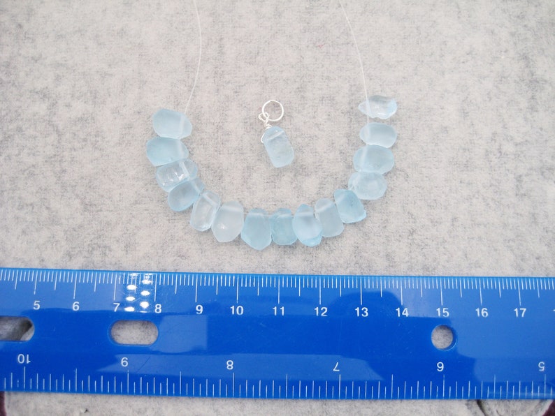 May include: A light blue sea glass necklace with a silver charm. The necklace is approximately 10 inches long and the beads are about 1/2 inch in diameter.