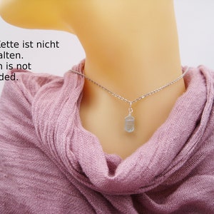 May include: A silver chain necklace with a light blue crystal pendant. The text "Die Kette ist nicht enthalten. Chain is not included." is visible in the image.
