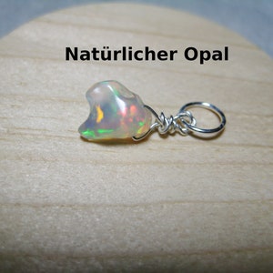 May include: A natural opal pendant with a silver wire wrap and a silver loop. The opal has a milky white base with flashes of green, yellow, and red. The text "Natürlicher Opal" is above the pendant.