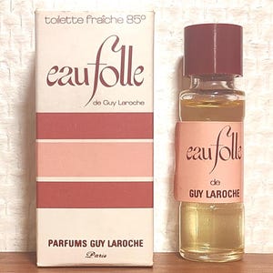 Peut inclure: Un flacon de parfum en verre avec un bouchon rouge foncé et une étiquette portant l'inscription eau folle de GUY LAROCHE, accompagné de sa boîte en carton rectangulaire assortie avec des rayures horizontales roses et rouges et le texte eau folle de Guy Laroche.