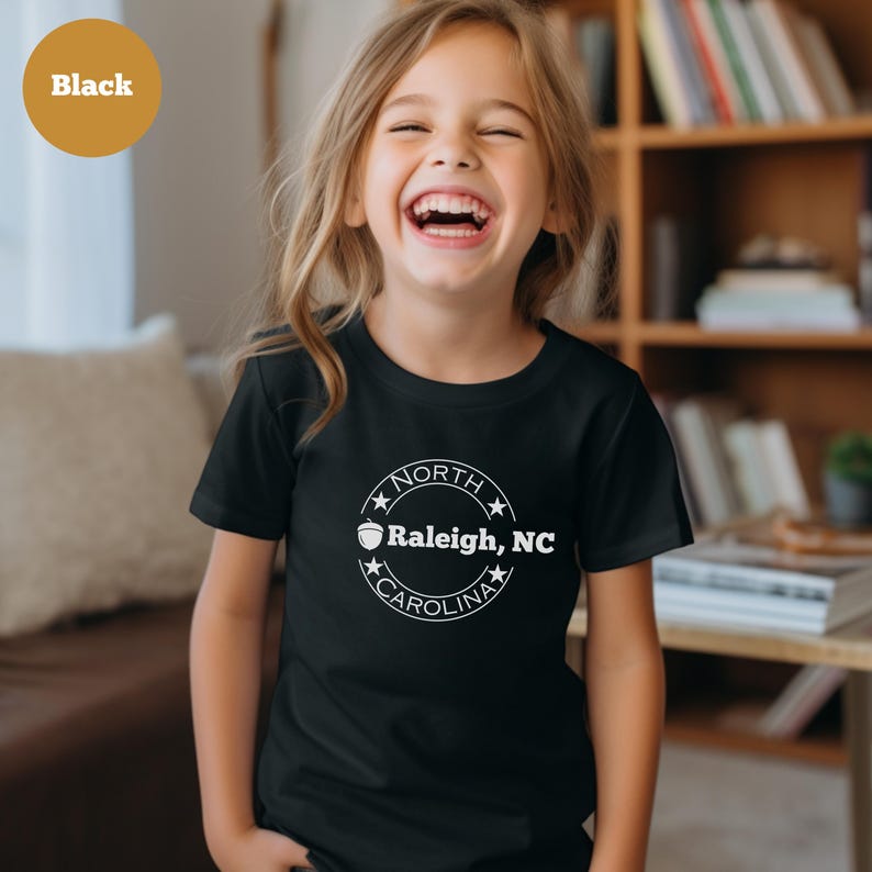 May include: A black t-shirt with a white circle design featuring a stylized acorn and the text "NORTH CAROLINA Raleigh, NC".