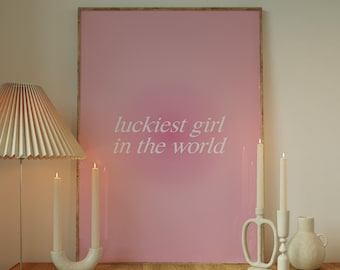 May include: A wooden table with a pink framed poster that says "luckiest girl in the world". There are three candles and a vase on the table.