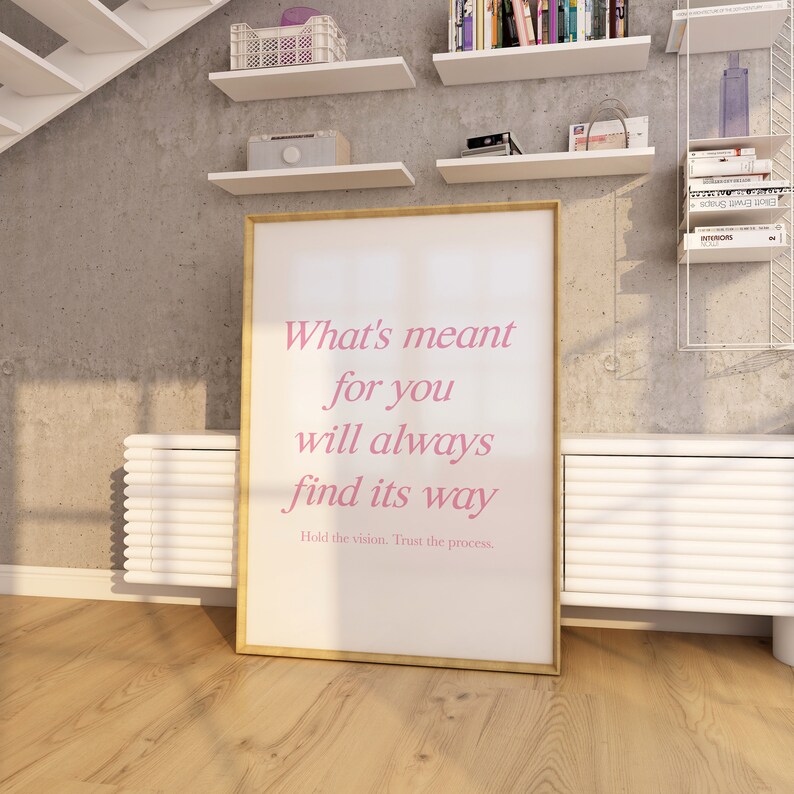 May include: A white framed poster with a pink text quote that reads 'What's meant for you will always find its way. Hold the vision. Trust the process.'