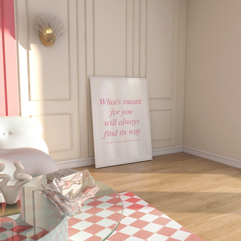 May include: A white framed poster with the text 'What's meant for you will always find its way.  Hold the vision. Trust the process.' in pink text on a white background.