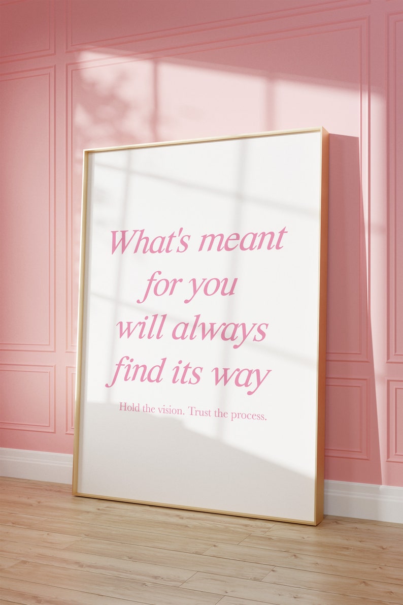 May include: A white framed poster with a pink quote that reads 'What's meant for you will always find its way. Hold the vision. Trust the process.'