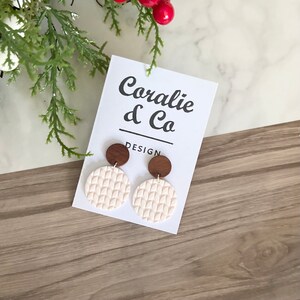 May include: A pair of white and brown statement earrings with a textured design. The earrings are displayed on a white card with the text "Coralie & Co. DESIGN".