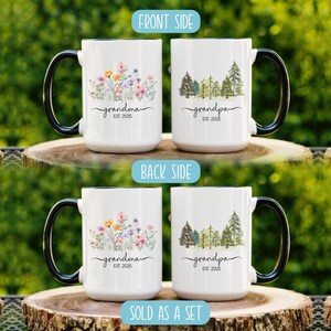 Op de afbeelding: Set van twee witte keramische mokken met zwarte handvatten. De ene mok heeft een bloemenontwerp met de tekst "grandma est. 2025". De andere mok heeft een bosontwerp met de tekst "grandpa est. 2025".