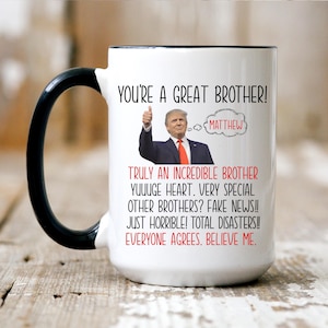 May include: White ceramic coffee mug with a black handle. The mug features a humorous image of a man with a thumbs up and the text "You're a great brother!" with the name "Matthew" in a speech bubble. The text below the image reads "Truly an incredible brother. Yuuuge heart. Very special other brothers? Fake news!! Just horrible! Total disasters!! Everyone agrees. Believe me."