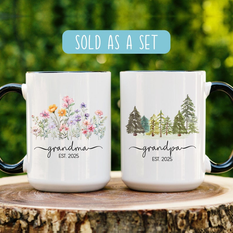 Op de afbeelding: Set van twee witte keramische mokken met zwarte handvatten. De mok aan de linkerkant heeft een bloemenmotief en de tekst "grandma est. 2025". De mok aan de rechterkant heeft een bosmotief en de tekst "grandpa est. 2025".