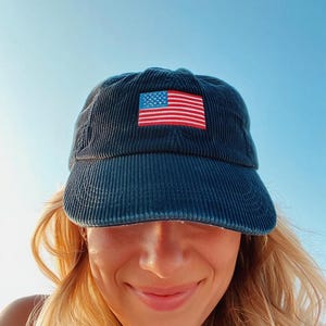 Pu&ograve; includere: Cappellino da baseball in velluto a coste blu navy con una toppa ricamata con la bandiera americana. Il cappellino ha una visiera curva e un classico design a sei pannelli. La toppa della bandiera mostra le stelle e le strisce in rosso, bianco e blu.