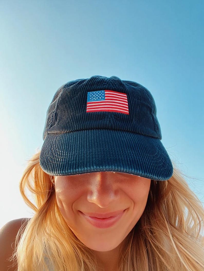 Pu&ograve; includere: Cappellino da baseball in velluto a coste blu navy con una toppa ricamata con la bandiera americana. Il cappellino ha una visiera curva e un classico design a sei pannelli. La toppa della bandiera mostra le stelle e le strisce in rosso, bianco e blu.