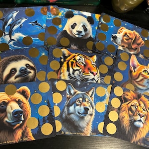 May include: Nine colorful cards with a variety of animals on them. Each card has a blue background with gold circles. The animals include a sloth, a tiger, a wolf, a lion, a panda, a cat, a dog, a bear, and dolphins.