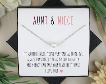 May include: A silver necklace with a single pearl pendant, presented in a black gift box. The box contains a card with the text "AUNT & NIECE" and a heartfelt message. Floral accents surround the box.
