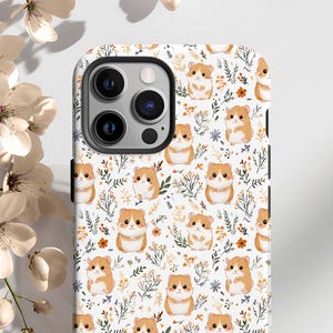 May include: A white phone case with a repeating pattern of cartoon hamsters, flowers, and leaves. The hamsters are brown and white, and the flowers are orange and yellow. The case has a camera cutout and black edges.