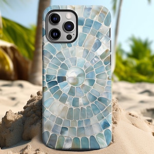Peut inclure: Une coque de smartphone avec un motif de mosaïque dans les tons de bleu et de blanc. L'étui présente un motif circulaire rappelant un coquillage ou un thème côtier. L'arrière-plan montre une plage de sable et des palmiers.