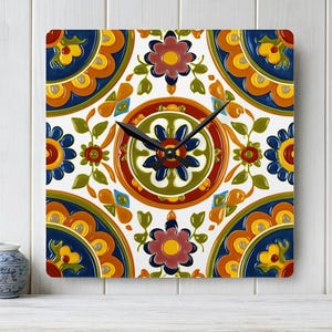 May include: Square wall clock with a colorful floral tile design. The clock face features a white background with a repeating pattern of blue, orange, yellow, and red flowers and leaves. Black clock hands indicate the time.